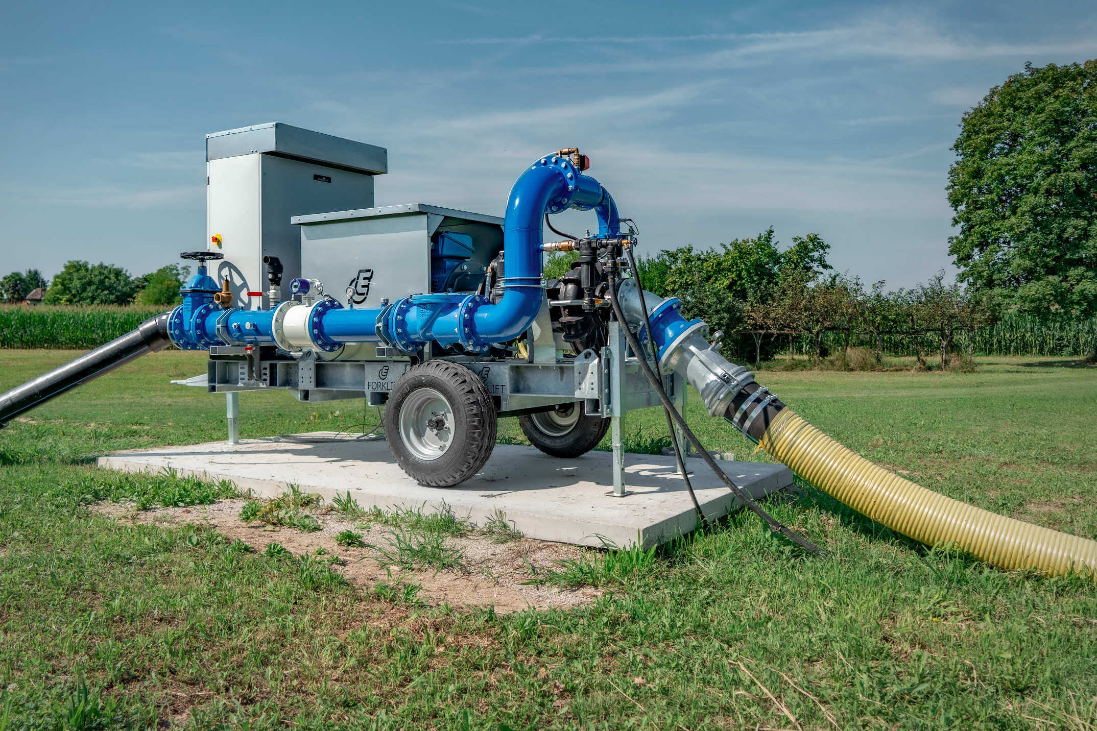 Euromacchine irrigation. Electric irrigation pump system with blue pipes installed on a trailer in a green field.